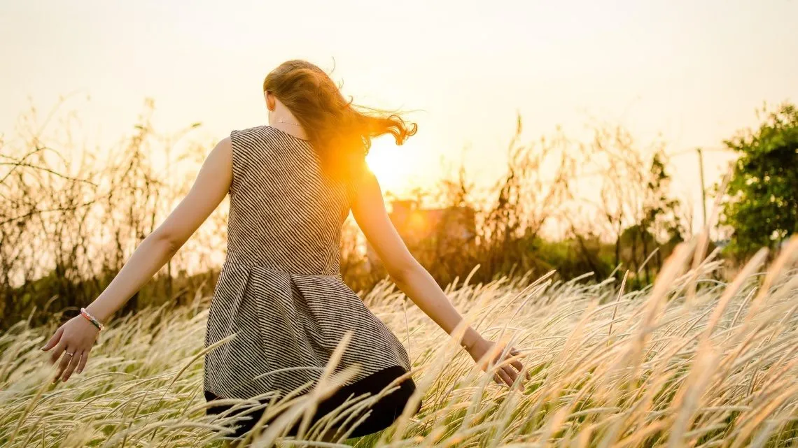 Frau geht bei Sonnenuntergang durch ein hohes Grasfeld