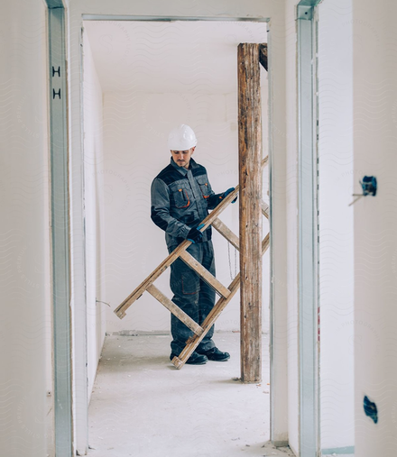 Ein Handwerker im Blaumann trägt eine Leiter durch eine Wohnung, die saniert wird.